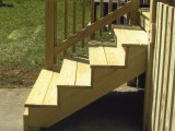 Side view of exterior stairs (right) which is open, hand rail on left side is visible and stair risers and view underneath exterior stairs is visible.